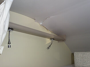 Decke mit sichtbarem Schaden bei zwei montierten Lampen.