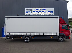 Roter LKW vor einer Werkstatt mit Schild 'Denis Gossler'.
