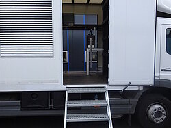 Ein LKW mit offener Seitentür und Metalltreppe.