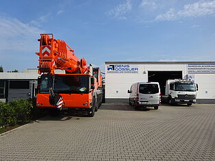 Großer orangefarbener Kran vor Werkstatt mit zwei Transportern