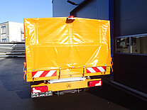 Oranger LKW mit Plane am Lagereingang.