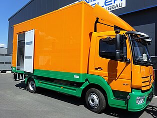 Orange-grüner Lieferwagen vor einem Gebäude geparkt.