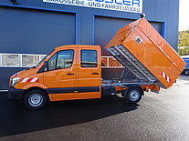 Oranger Kipper-Lkw mit angehobener Ladefläche vor Gebäude.