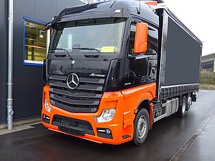 Orange-schwarzer LKW neben einem Gebäude geparkt.