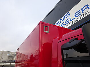 Roter LKW in der Nähe eines Gebäudes mit Schild.