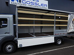 Ein LKW mit offener Seitenwand und Holzlatten im Aufbau.