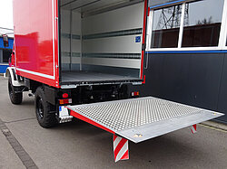Roter LKW mit offener hinterer Laderampe auf Straße.