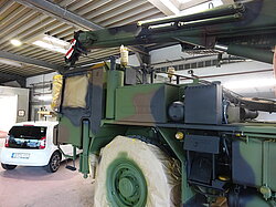 Grünes Militärfahrzeug neben weißem Auto in Werkstatt