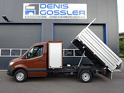 Brauner Kipper vor einer Werkstatt mit Schild 'Denis Gossler'.