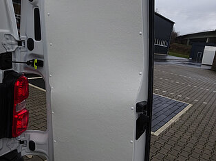 Offene Hecktür eines weißen Vans auf einem Parkplatz.