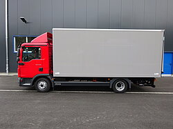 Roter LKW mit grauem Aufbau vor Gebäude