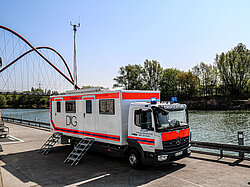 Einsatzleitfahrzeug an einem Fluss mit Brücke.