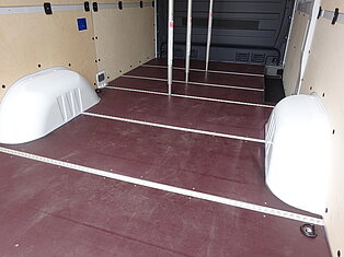 Innenraum eines leeren Vans mit Holzverkleidung und Radkästen.
